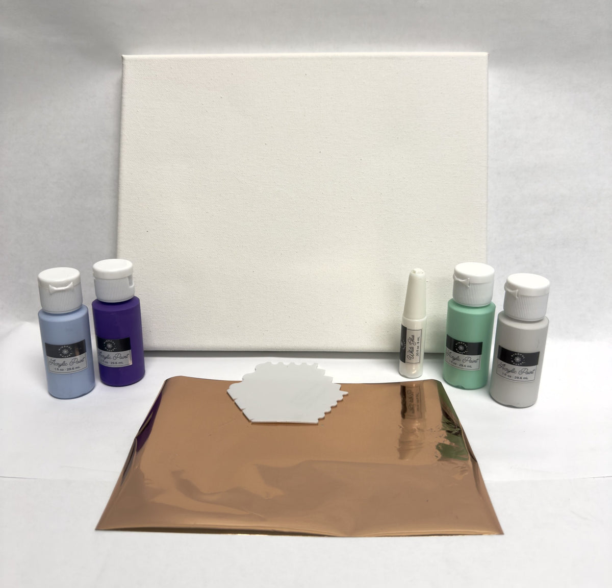 Art supplies including paint bottles, a canvas, and metallic paper on a white surface.