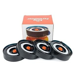 Four easy-to-use black fermentation lids with orange airlocks, arranged in a group in front of a colorful product box featuring the brand name.
