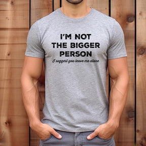 Person wearing a gray t-shirt with humorous text design against a wooden background