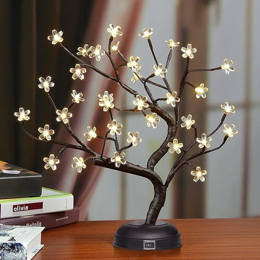 Decorative LED tree lamp on a wooden surface with books in the background