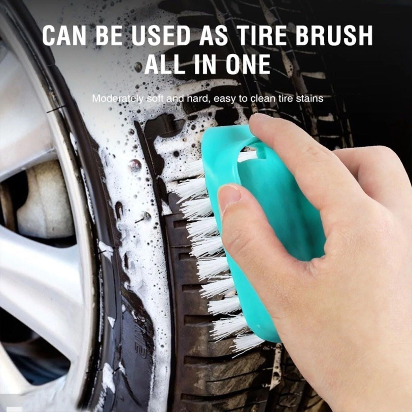 A hand holding a turquoise cleaning brush is scrubbing a car tire covered in soap suds, showcasing the brush's white bristles designed for effective tire cleaning.