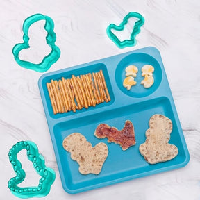 A blue divided tray holds two shaped pieces of bread with a spread, pretzel sticks, and cheese snack figures, surrounded by four fun-shaped green sandwich cutters.