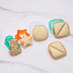 Assorted sandwich shapes include a gingerbread man, star, and a rectangular shape, alongside two sandwich seals in green and orange, with one sandwich cut in half to show the filling.