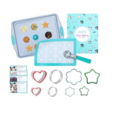 A light blue baking tray holds colorful cookies shaped like stars, flowers, and circles, alongside a silicone mat with circular molds, cookie cutters in various shapes (star, heart, flower), a metal spatula, and a baking instruction booklet with a playful design.