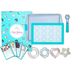 Colorful accessories for cookie baking including a turquoise silicone baking mat with circular outlines, a silver baking sheet, a metal scooper, and various cookie cutters in star, heart, and flower shapes, all arranged on a light background.
