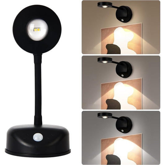 Black wireless motion sensor spotlight with a round head and flexible arm, designed to illuminate pictures or artwork. The spotlight features three different dimmable color options and is mounted on a base with a motion sensor.
