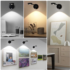 Four black wireless motion sensor spotlights are mounted on walls, each illuminating different artwork and objects in various lighting colors. The arrangement showcases the versatility of the spotlight, with two functional angles highlighting details of framed pictures and decorative items in a stylish interior setting.