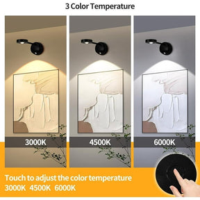 Three orientations of a wireless motion sensor picture spotlight mounted on walls, illuminating an artwork with varying light temperatures (3000K, 4500K, and 6000K), depicted in black against a neutral background with a touchpad interface shown for adjusting colors.