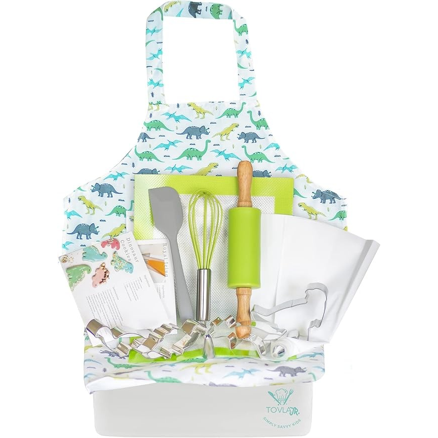 Colorful dinosaur-themed apron with a variety of baking tools including a rolling pin, spatula, whisk, cookie cutters, and baking sheet, all arranged neatly in a white container.