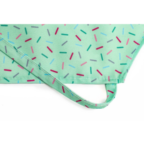 The mint green apron features a playful sprinkle pattern in various colors, including pink, light blue, and dark green, along with a coordinating strap for adjustment. The texture appears smooth, suitable for kids' cooking activities.