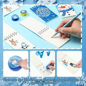A hand writes in a notepad featuring colorful winter-themed characters, alongside a festive notebook, pencil sharpener, and decorative stickers. The scene is set on a light blue background with snowflake accents.