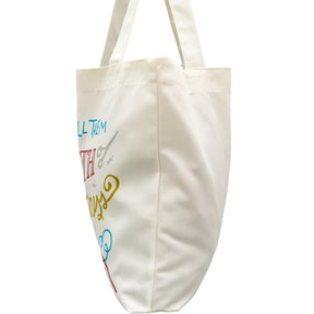 Side view of a cream-colored canvas tote bag featuring colorful graphics and text related to crafting, with sturdy handles for easy carrying.