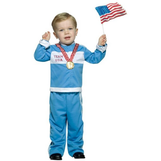 Toddler wearing a light blue athletic costume with white stripes and the text "TEAM USA," holding a small American flag in one hand and displaying two red and gold medal ribbons around the neck.