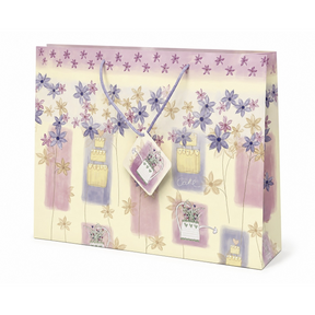 The gift bag features a pastel floral design with purple and yellow flowers, adorned with illustrated cake and flower pot motifs. It includes twisted handles for easy carrying and is finished with a high gloss for a polished appearance.