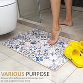 A foot is placed on a colorful, patterned doormat featuring various geometric designs in blue and grey, positioned on a light tile floor, with yellow clogs nearby.