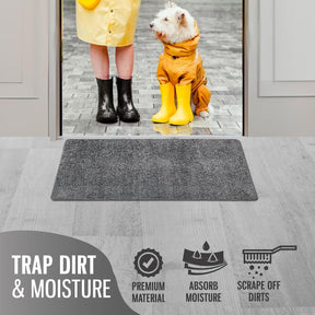 Gray doormat positioned on a wooden floor, showing a textured surface designed for moisture absorption and dirt trapping. The background features a person in yellow rain gear standing with a dog, highlighting the doormat's use in an entryway.
