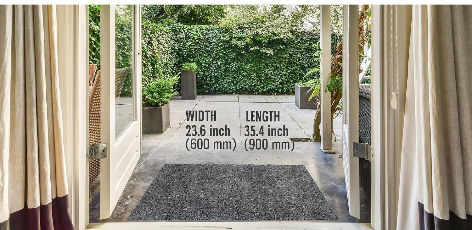 The gray doormat measures 23.6 inches in width and 35.4 inches in length, positioned at an entrance surrounded by greenery and patio tiles. It blends seamlessly with the outdoor setting.