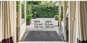 The gray doormat measures 23.6 inches in width and 35.4 inches in length, positioned at an entrance surrounded by greenery and patio tiles. It blends seamlessly with the outdoor setting.
