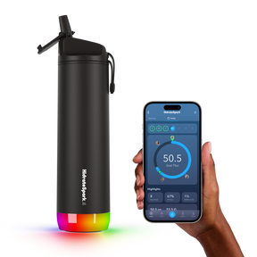 The sleek black 21 OZ HidrateSpark Pro Smart Water Bottle features a colorful, illuminated base and a convenient flip-top lid. Next to the bottle, a hand holds a smartphone displaying the HidrateSpark app interface with hydration tracking details.