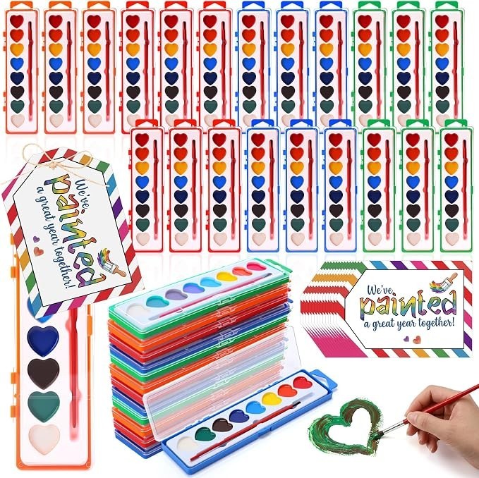 A colorful assortment of heart-shaped watercolor paint sets in various colors, neatly arranged with some sets stacked and a paintbrush shown in use creating a green heart. Includes playful branding cards that read "We've painted a great year together!"