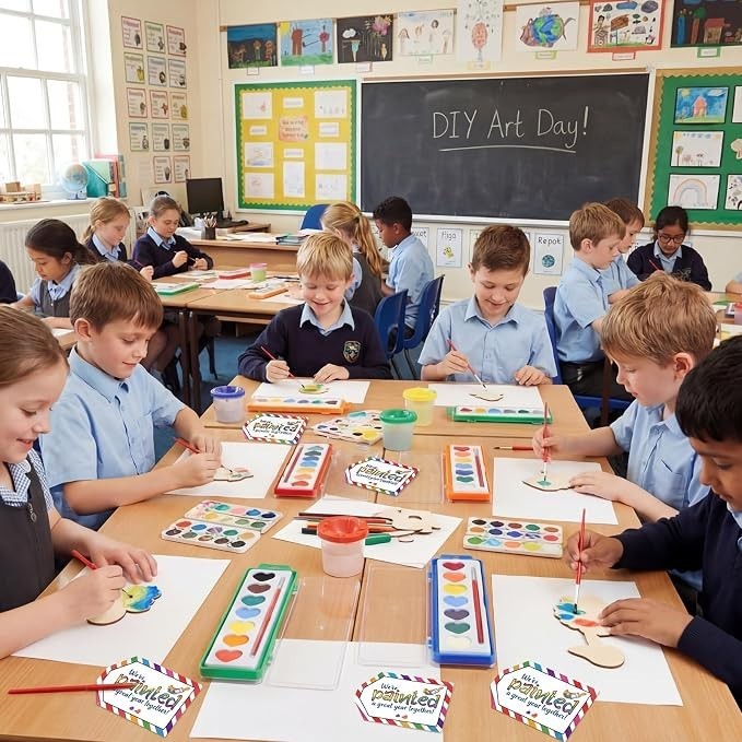 Children engaged in an art class, using heart-shaped watercolor paints at individual tables. Each child is focused on their artwork, with colorful paint palettes and brushes on the tables, and art supplies scattered around in a bright classroom setting.