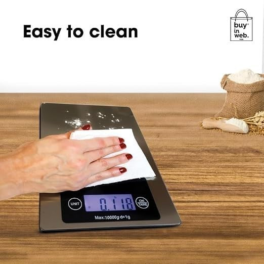 A hand with manicured nails is wiping the stainless steel surface of the digital food scale, which displays a measurement of 0.118. A burlap sack filled with flour is partially visible in the background, along with a wooden countertop.