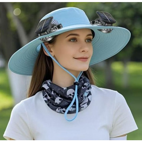 A woman is wearing a light blue unisex solar fan hat featuring solar panels on each side, along with a black and white patterned neck gaiter. The hat has a wide brim and a chin strap, set against a green outdoor background.