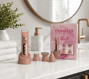 The cordless rechargeable trimmer kit is showcased in a soft pink color and features a sleek design with a base station. Surrounding it are four additional attachment heads along with a pink packaging box, all set against a stylish bathroom countertop background.