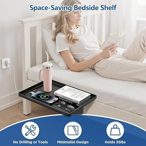 A woman is comfortably seated on a bed, reading a book while using the clamp-on bedside shelf, which holds a smartphone, a pair of glasses, and a pink water tumbler. The shelf is positioned against the bed, demonstrating its space-saving, minimalist design.