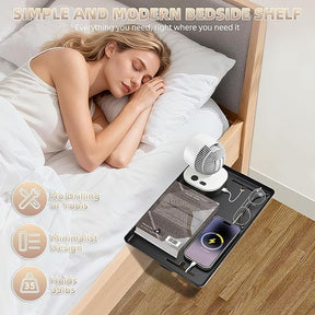 A woman is sleeping in bed next to a black clamp-on bedside shelf holding a phone with a charging icon, a pair of glasses, a book, and a small fan. The shelf displays a modern minimalist design, seamlessly integrated into the bed's side.