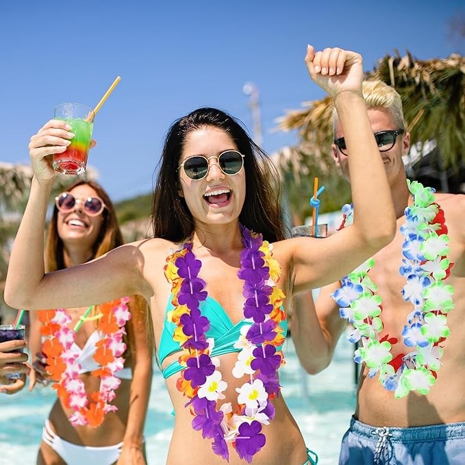 Three young adults at a beach party, wearing colorful tropical lei necklaces, with drinks in hand. They are smiling and celebrating under a clear blue sky.