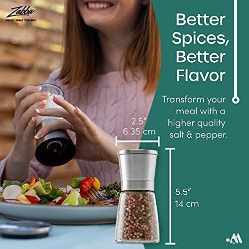 A person is using a salt and pepper shaker set at a dining table, with the salt shaker in their right hand and a visible meal on the table. The shakers feature a modern design, and there is text beside the shaker detailing their dimensions.