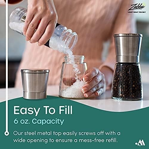 A person fills a glass salt shaker with salt, showcasing the shaker's wide opening and metal top. The set includes a pepper shaker alongside, highlighting its sleek design and 6 oz. capacity.