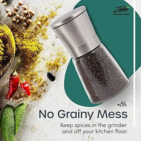 Stainless steel and glass salt and pepper grinder shown with peppercorns inside, set against a colorful backdrop of spices, herbs, and chili peppers. Text highlights "No Grainy Mess" and emphasizes keeping spices contained.