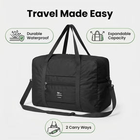 The black Foldable Weekender Tote Bag features durable, waterproof material and an expandable design, with two visible carry options: short handles and a detachable shoulder strap. A front zippered pocket and a brand logo are also visible.