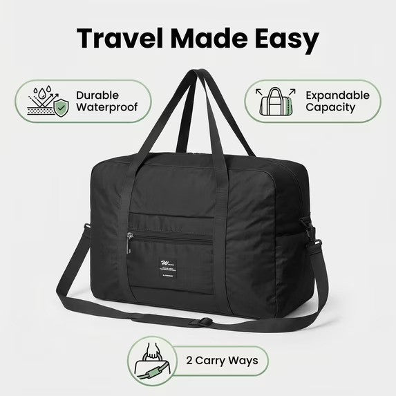 The black Foldable Weekender Tote Bag features durable, waterproof material and an expandable design, with two visible carry options: short handles and a detachable shoulder strap. A front zippered pocket and a brand logo are also visible.