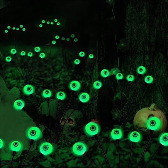 Green LED eyeball lights are arranged on long, slender stems in a dark, eerie setting, creating a spooky atmosphere with a background featuring a skull and pumpkins.