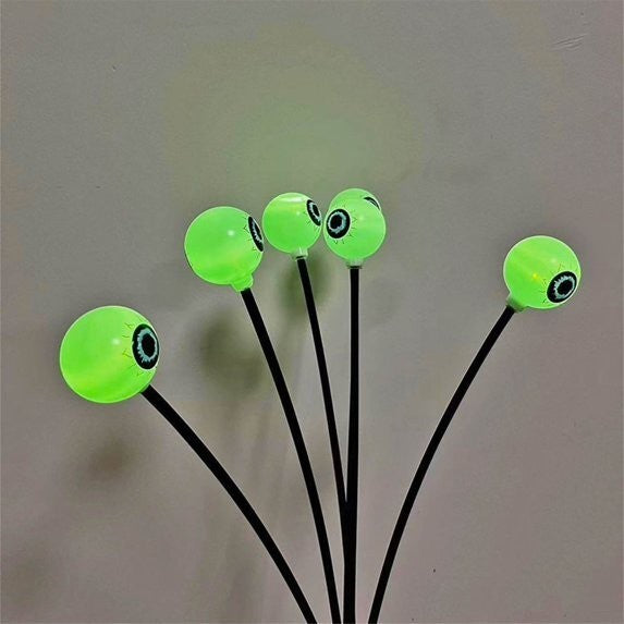 Five glowing green eyeball lights with black pupils are mounted on thin black stems, arranged in a cluster against a neutral background.