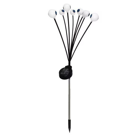 The product features six white eyeball-shaped lights attached to flexible black stems, all anchored to a metal stake with a solar panel unit at the base. The design creates a spooky and playful look, perfect for Halloween decorations.