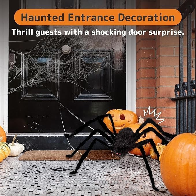 A large, hairy black spider with glowing red eyes is positioned in front of a black door surrounded by carved pumpkins and spiderwebs, creating a spooky Halloween entrance. The scene conveys a festive, haunted atmosphere perfect for welcoming guests.