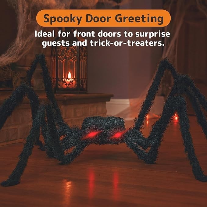 The image features a large, hairy black spider prop with glowing red eyes, positioned on a wooden floor in a cozy, dimly lit setting that includes a decorative lantern in the background. The spider's limbs are spread wide, emphasizing its spooky appearance, ideal for Halloween decorations.