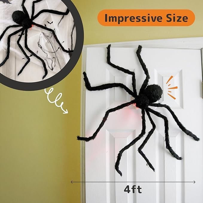 Large black hairy spider prop, measuring 4 feet across, with illuminated red LED eyes, positioned on a white door against a light-colored wall. The spider's outstretched legs and body texture are clearly visible, enhancing its spooky appearance.