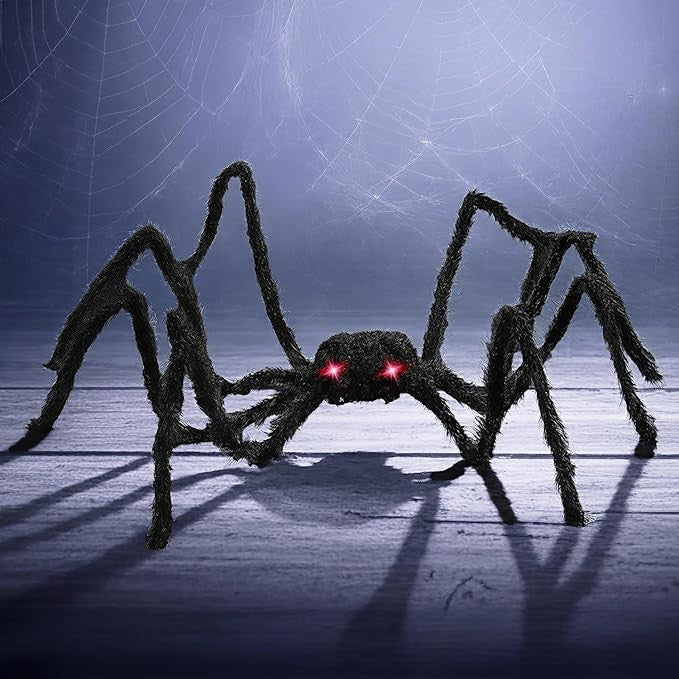 The hairy black spider prop features red LED lights for eyes and has long, flexible legs, creating a spooky appearance. It is set against a dark, atmospheric background with subtle spiderweb details.