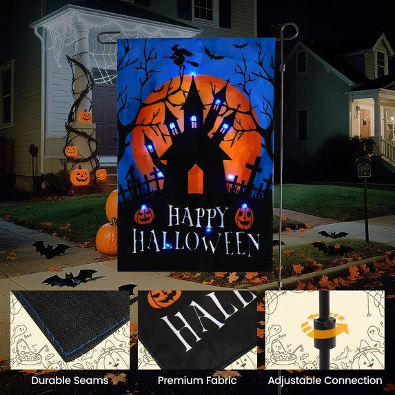 Halloween-themed garden flag featuring a spooky silhouette of a haunted house against an orange full moon, with the text "HAPPY HALLOWEEN" in white. The background is dark blue with bats, and the flag is displayed outdoors with decorative pumpkins nearby.