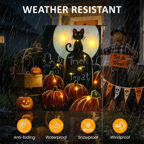 A brightly colored Halloween garden flag features a black cat, pumpkins, and the words "Trick or Treat," illuminated by LED lights while surrounded by raindrops, emphasizing its weather-resistant qualities. The scene includes a scarecrow and additional Halloween decorations in the background.
