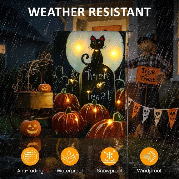 A brightly colored Halloween garden flag features a black cat, pumpkins, and the words "Trick or Treat," illuminated by LED lights while surrounded by raindrops, emphasizing its weather-resistant qualities. The scene includes a scarecrow and additional Halloween decorations in the background.