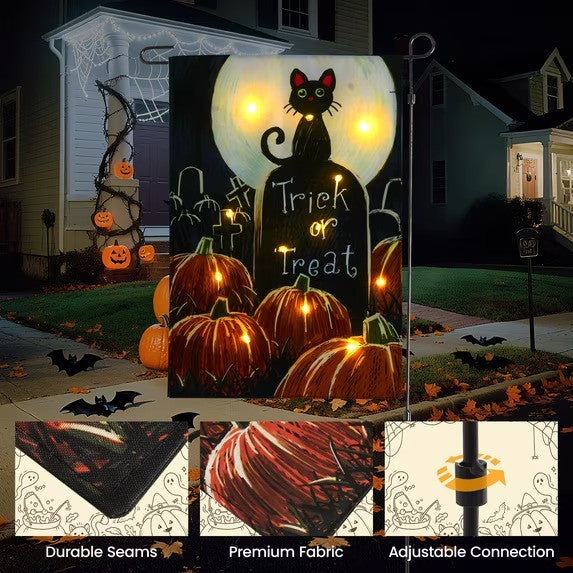 The garden flag features a playful Halloween design with a black cat sitting on a tombstone, illuminated by LED lights, alongside festive pumpkins and the words "Trick or Treat." This flag is displayed in a nighttime setting, enhancing its visibility and appeal.