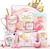 The birthday gift set features a pink-themed collection, including a mug that reads "NOT A DAY OVER FABULOUS," a lavender scented candle, a pouch with "Queen of Everything" printed on it, and several decorative items like a crown and greeting cards. The set is arranged with various accessories, showcasing a fun and celebratory aesthetic.