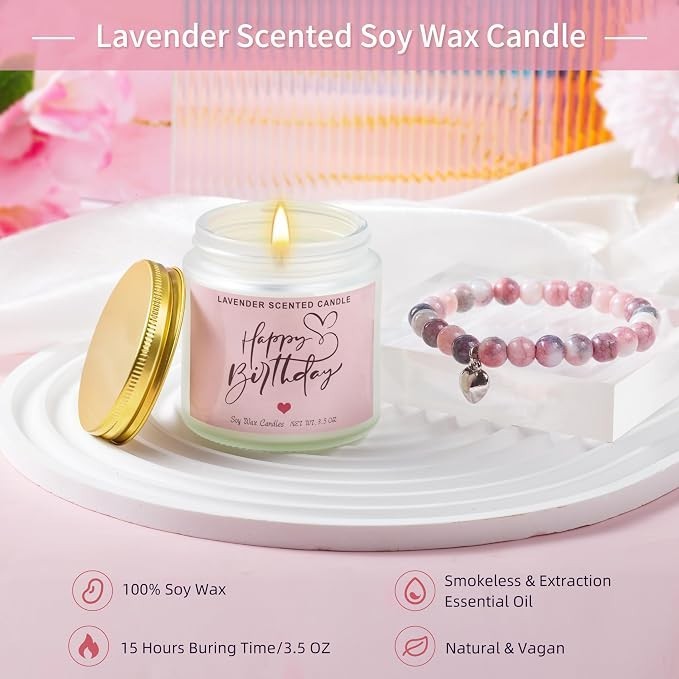 Lavender scented soy wax candle with a gold-colored lid featuring "Happy Birthday" text on a pink label, placed next to a beaded bracelet in soft pink and purple tones. The candle is lit and displayed on a round white plate.