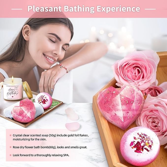 A woman with long dark hair is enjoying a relaxing moment, leaning slightly on a wooden tray filled with a pink heart-shaped soap, a white bath bomb, and a candle with "Happy Birthday" on it, accompanied by fresh pink roses and delicate petals.